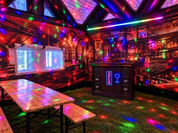 Full Party Package – pub interior Full Party Package inside an inflatable pub, with wooden tables, benches, a Jukebox Bar and colourful lighting